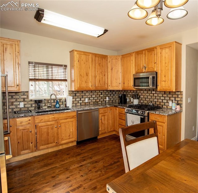 kitchen with dark wood-type flooring, sink, dark stone counters, and appliances with stainless steel finishes