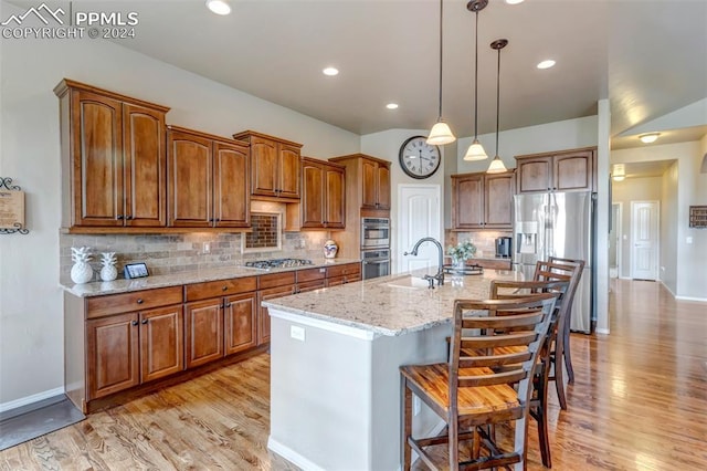 kitchen featuring light stone counters, stainless steel appliances, sink, decorative light fixtures, and an island with sink