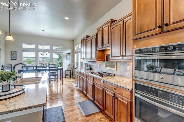 kitchen featuring sink, decorative light fixtures, light stone countertops, a notable chandelier, and stainless steel appliances