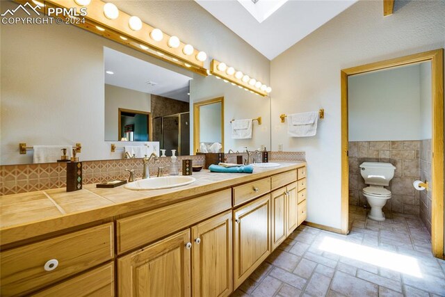 bathroom with toilet, tile walls, vaulted ceiling with skylight, oversized vanity, and dual sinks