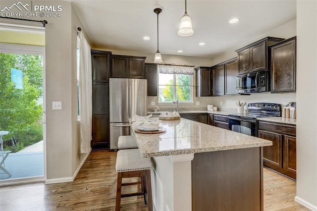 kitchen with pendant lighting, stainless steel fridge, a center island, light stone counters, and black electric range