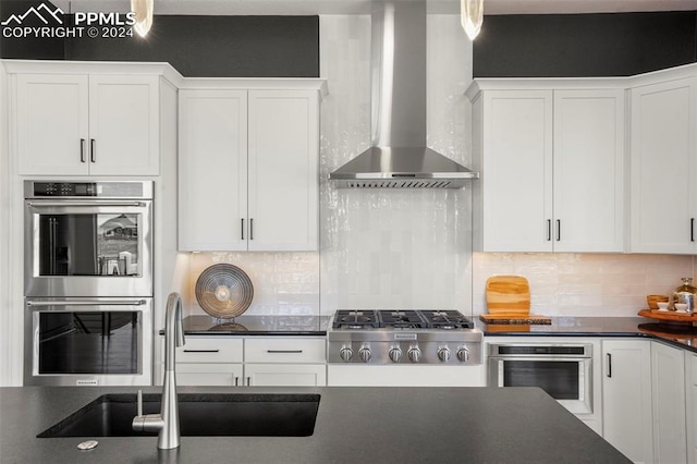 kitchen with white cabinets, wall chimney exhaust hood, backsplash, and appliances with stainless steel finishes