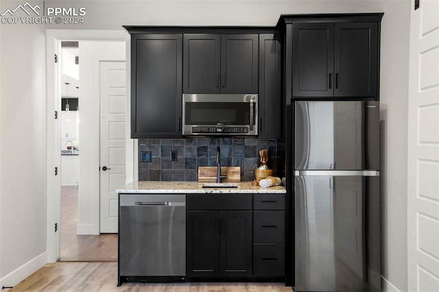 kitchen with backsplash, sink, light wood-type flooring, appliances with stainless steel finishes, and light stone counters