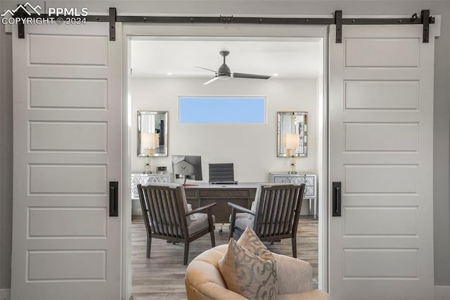 home office with a barn door, ceiling fan, and hardwood / wood-style floors