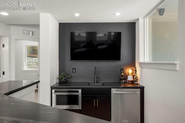 bar with sink, stainless steel appliances, and dark brown cabinets