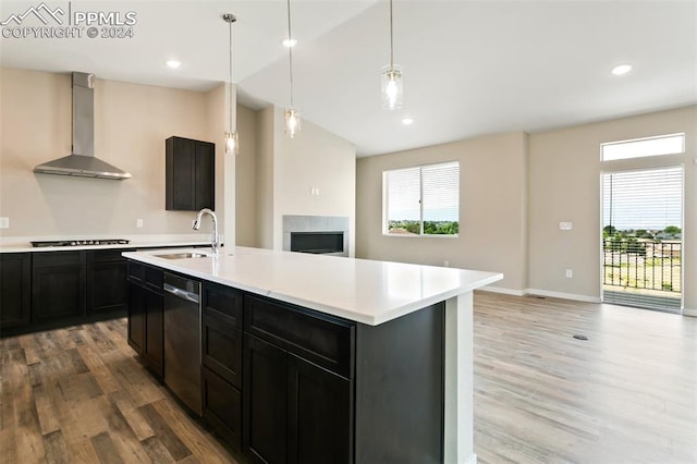 kitchen featuring wall chimney range hood, light hardwood / wood-style flooring, a kitchen island with sink, gas stovetop, and sink