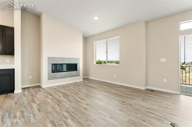 unfurnished living room with a healthy amount of sunlight, a tiled fireplace, and light hardwood / wood-style flooring