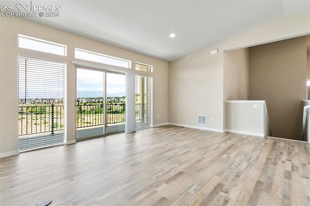 unfurnished room with a healthy amount of sunlight, vaulted ceiling, and light hardwood / wood-style floors