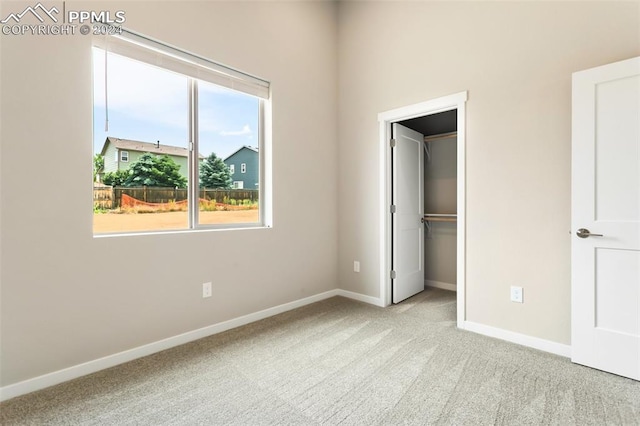 unfurnished bedroom with a spacious closet, a closet, and light colored carpet