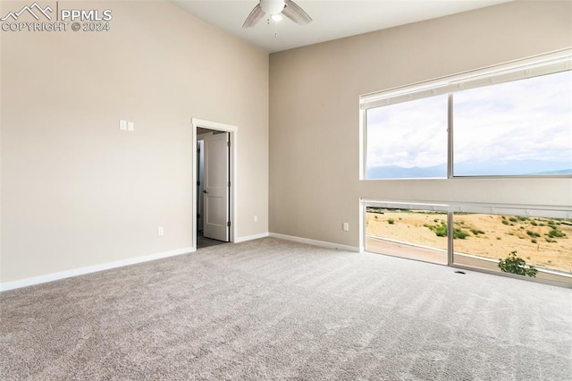 carpeted spare room with a towering ceiling and ceiling fan