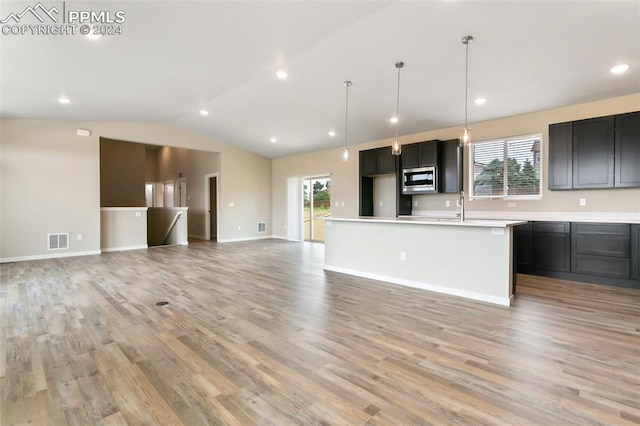 kitchen with light hardwood / wood-style floors, vaulted ceiling, stainless steel microwave, a kitchen island, and hanging light fixtures