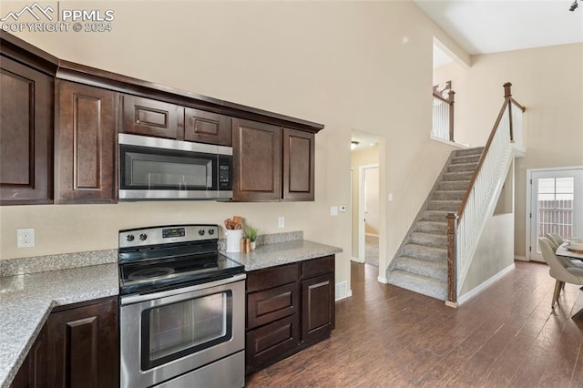 kitchen featuring light stone countertops, beamed ceiling, dark brown cabinetry, dark hardwood / wood-style flooring, and appliances with stainless steel finishes