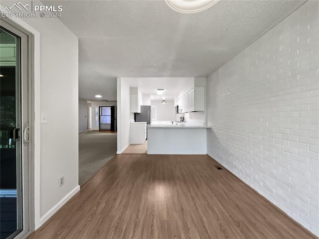 unfurnished living room featuring sink, a textured ceiling, dark wood-type flooring, and brick wall