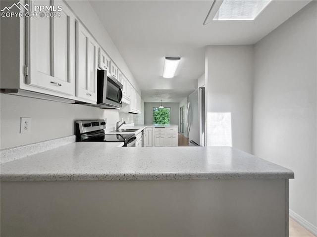 kitchen featuring kitchen peninsula, light stone counters, stainless steel appliances, sink, and white cabinets