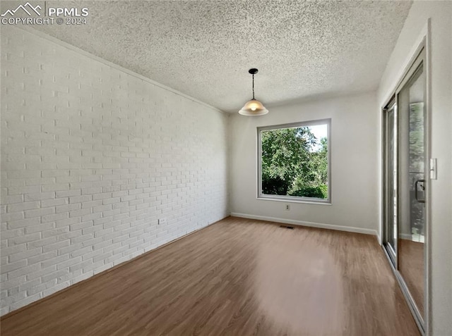 unfurnished dining area featuring brick wall, a textured ceiling, and hardwood / wood-style flooring