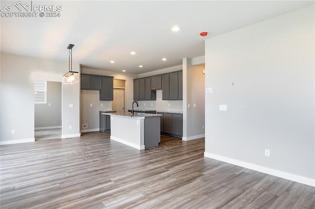 kitchen with light stone counters, an island with sink, wood-type flooring, sink, and gray cabinetry