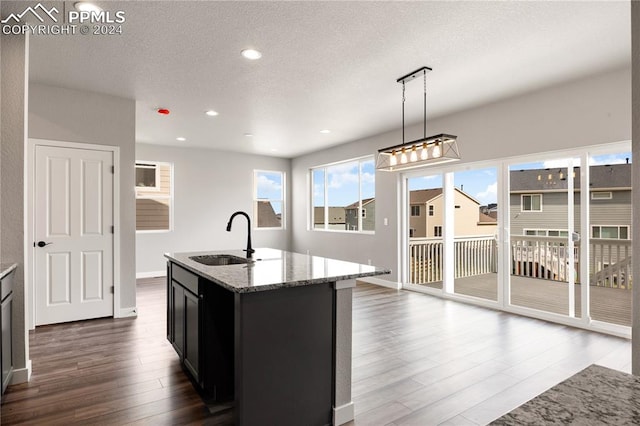 kitchen with decorative light fixtures, an island with sink, sink, a textured ceiling, and dark wood-type flooring