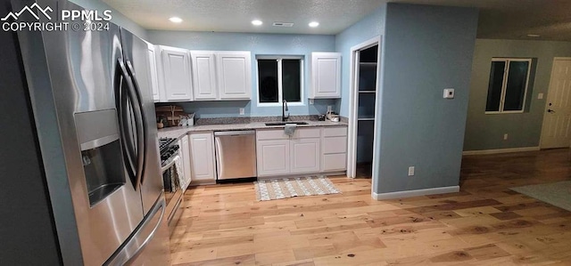 kitchen with light wood-type flooring, stainless steel appliances, white cabinetry, and sink