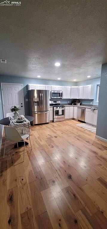 kitchen featuring white cabinetry, stainless steel appliances, a textured ceiling, and light hardwood / wood-style floors