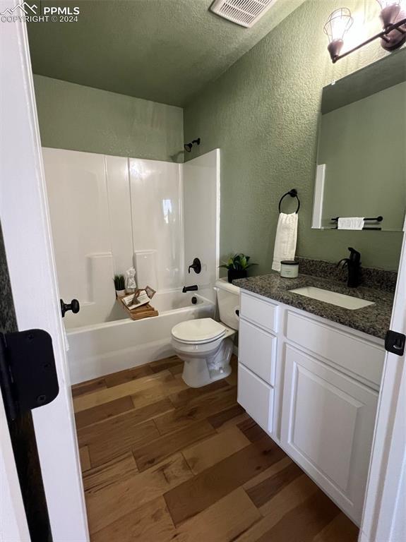 full bathroom with vanity, a textured ceiling, shower / washtub combination, hardwood / wood-style floors, and toilet