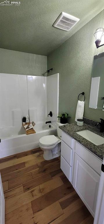 full bathroom with vanity, hardwood / wood-style flooring, toilet, a textured ceiling, and shower / bath combination