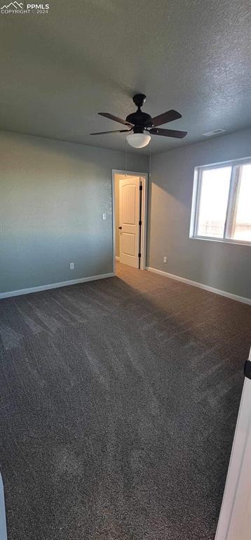 empty room featuring ceiling fan, dark carpet, and a textured ceiling