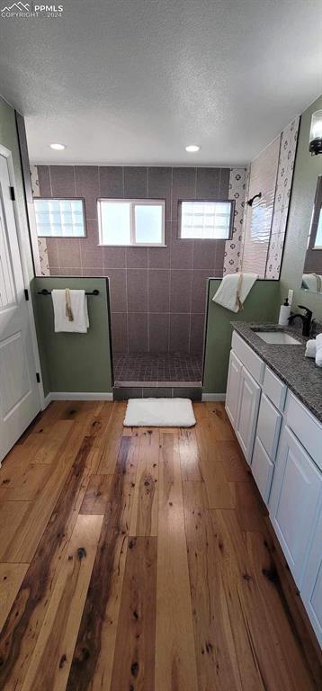 bathroom featuring wood-type flooring, vanity, a textured ceiling, and a tile shower