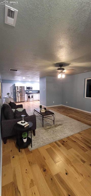 living room with a textured ceiling, hardwood / wood-style flooring, and ceiling fan