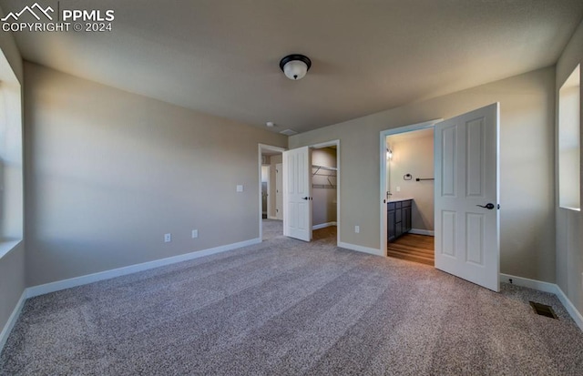 unfurnished bedroom featuring ensuite bath, carpet, a closet, and a walk in closet