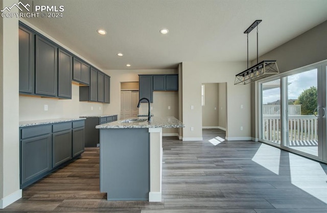 kitchen featuring decorative light fixtures, light stone counters, dark hardwood / wood-style floors, a kitchen island with sink, and sink