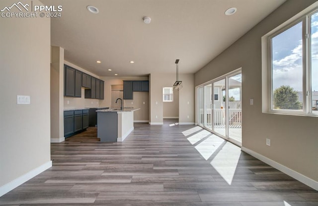 kitchen featuring light stone countertops, a center island with sink, a wealth of natural light, and dark wood-type flooring