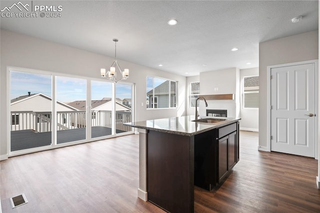 kitchen with a wealth of natural light, a kitchen island with sink, sink, pendant lighting, and a chandelier