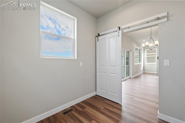 hall featuring a barn door, dark wood-type flooring, and a notable chandelier