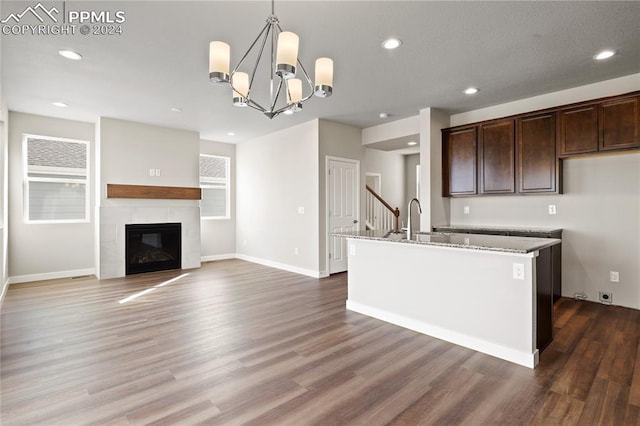 kitchen with hanging light fixtures, dark hardwood / wood-style floors, dark stone countertops, a fireplace, and dark brown cabinets