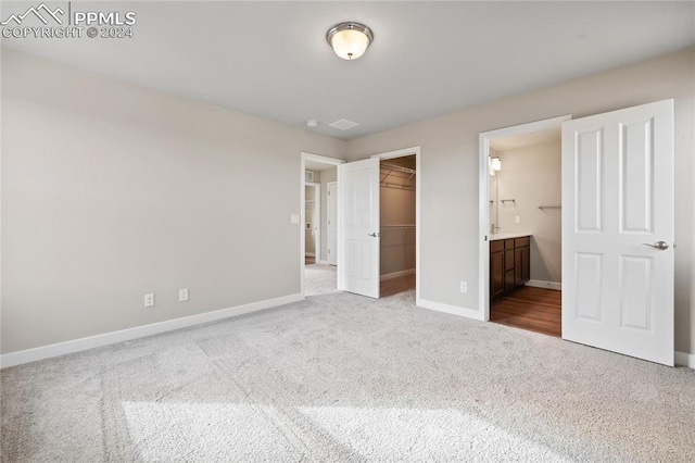 unfurnished bedroom featuring connected bathroom, a spacious closet, a closet, and carpet