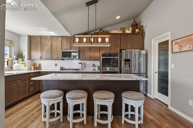 kitchen with decorative backsplash, stainless steel appliances, vaulted ceiling, decorative light fixtures, and a kitchen island