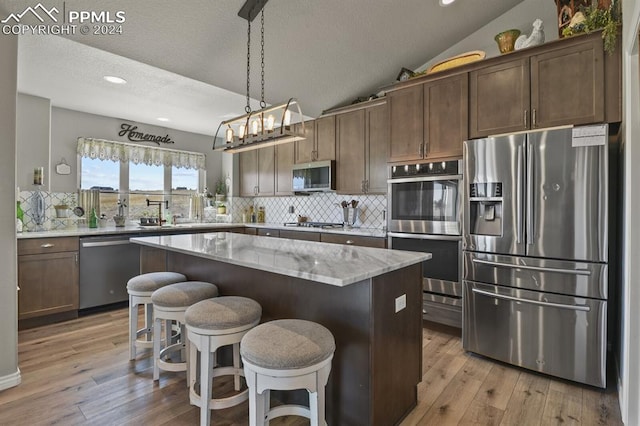 kitchen with a center island, vaulted ceiling, decorative light fixtures, dark brown cabinets, and appliances with stainless steel finishes