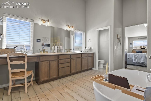 bathroom featuring a towering ceiling, a tub to relax in, vanity, hardwood / wood-style flooring, and toilet