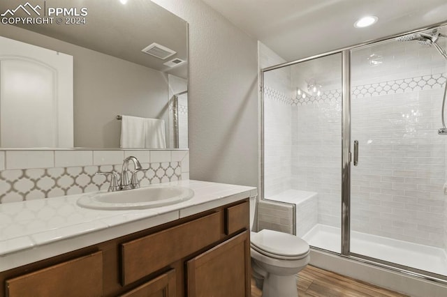 bathroom featuring backsplash, walk in shower, vanity, wood-type flooring, and toilet