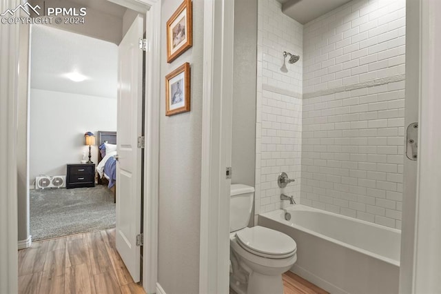 bathroom featuring wood-type flooring, toilet, and tiled shower / bath