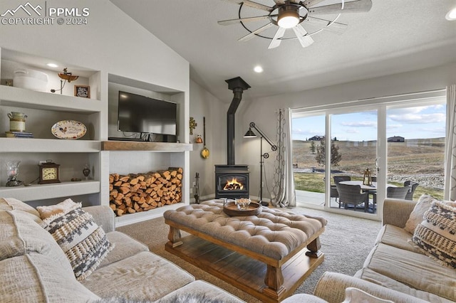 carpeted living room featuring built in shelves, ceiling fan, a wood stove, and lofted ceiling