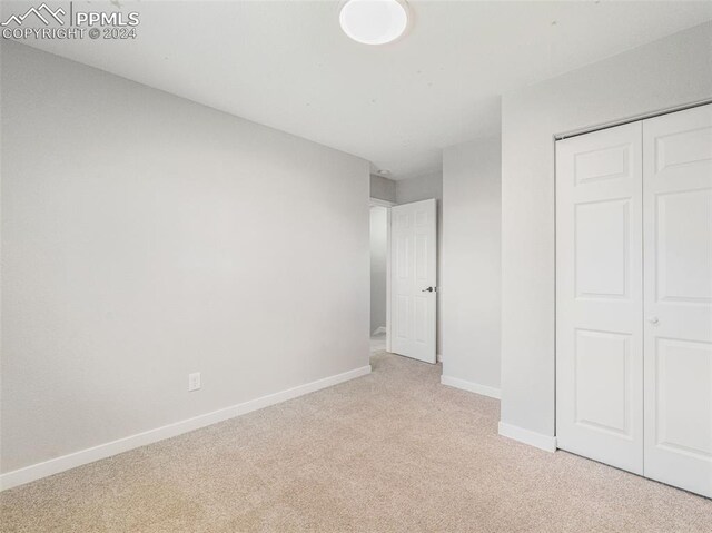 unfurnished bedroom with light colored carpet and a closet