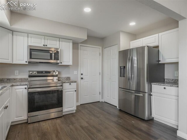 kitchen with appliances with stainless steel finishes, white cabinetry, dark hardwood / wood-style floors, and light stone countertops