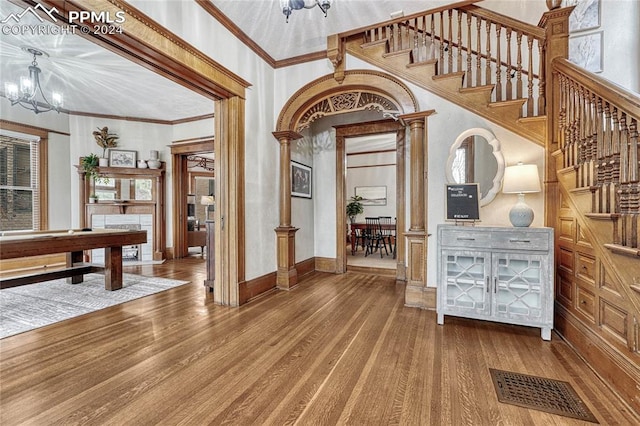 foyer featuring wood finished floors, crown molding, a chandelier, stairs, and ornate columns