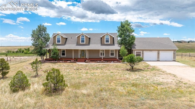 new england style home featuring a front yard, covered porch, a rural view, and a garage