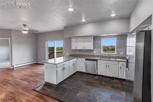 kitchen with kitchen peninsula, sink, baseboard heating, appliances with stainless steel finishes, and white cabinetry