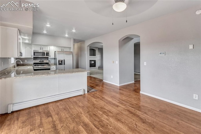 kitchen featuring kitchen peninsula, light stone countertops, stainless steel appliances, a baseboard heating unit, and white cabinets