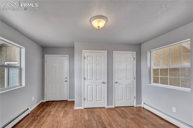 unfurnished bedroom featuring hardwood / wood-style flooring, two closets, and a baseboard radiator