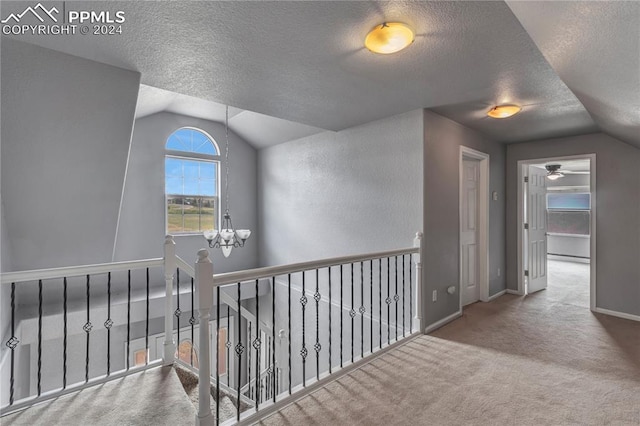 corridor with a textured ceiling, carpet floors, vaulted ceiling, and an inviting chandelier