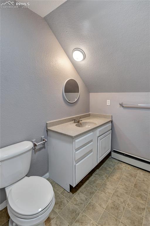 bathroom with baseboard heating, a textured ceiling, vaulted ceiling, toilet, and vanity